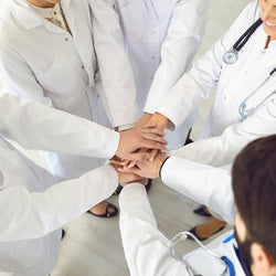 Image of Five doctors and nurses wearing white lab coats and stethoscopes putting their clean hands together before starting their morning rounds.