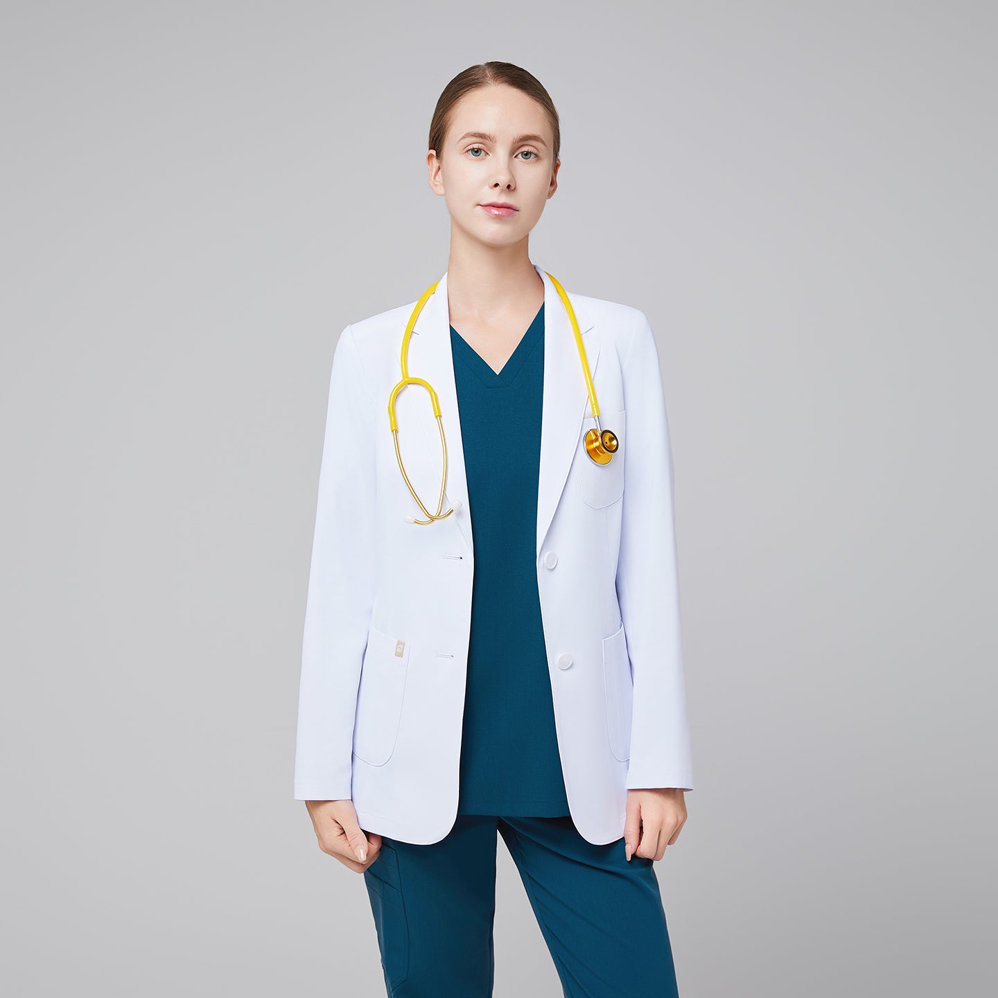 Female medical professional wearing a white lab coat over teal scrubs, with a yellow stethoscope around her neck, standing in a neutral pose,White