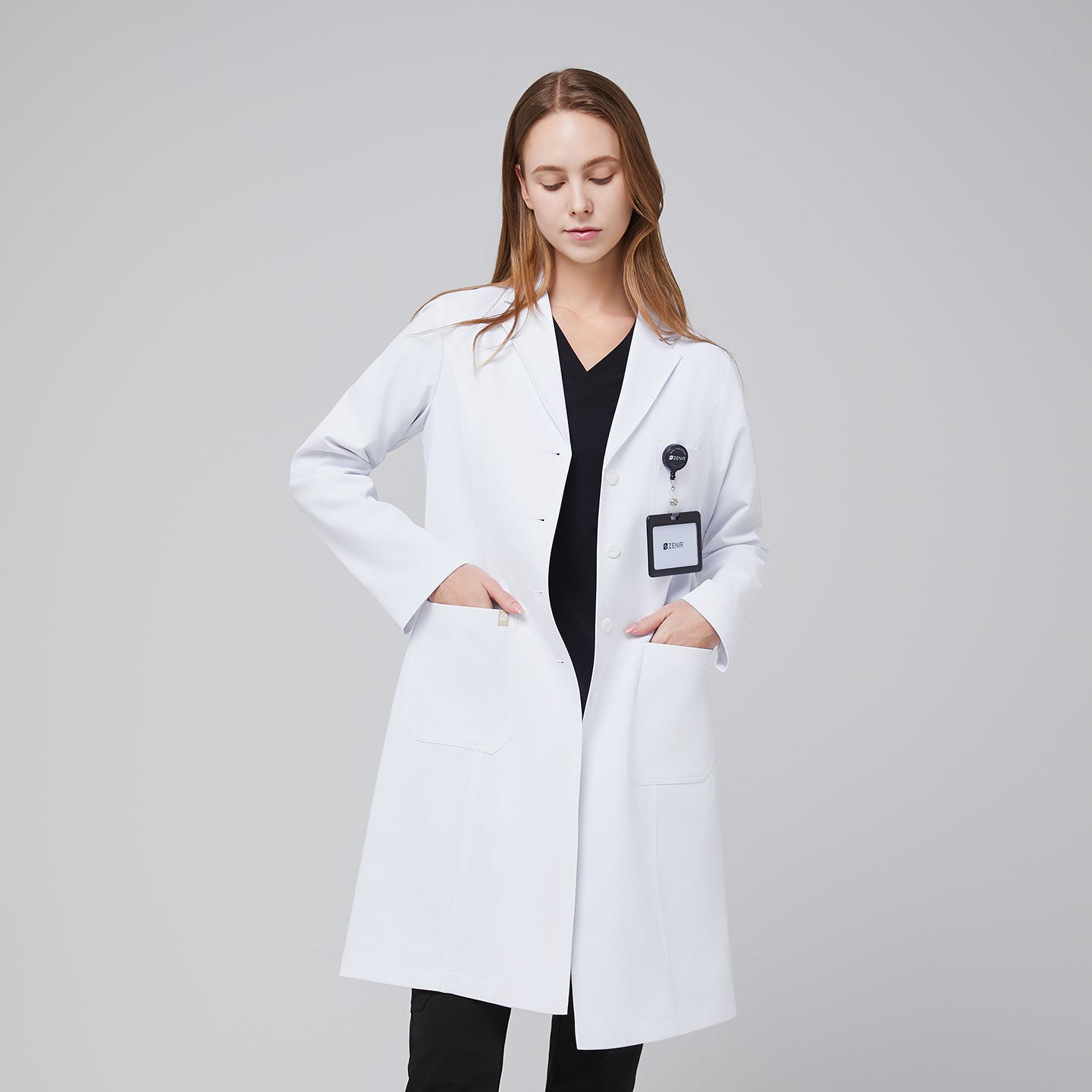 Female doctor wearing a white lab coat with hands in pockets and an ID badge displayed,White