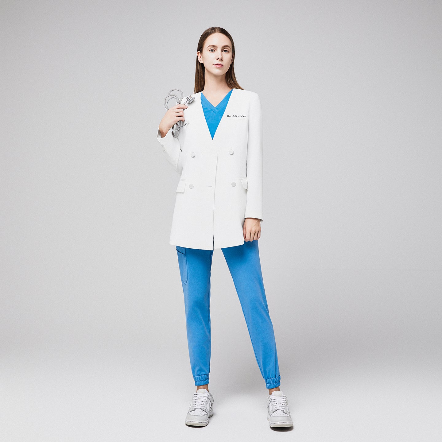 Female doctor in a white double-breasted lab coat with embroidered name, blue scrubs, and sneakers, holding a stethoscope, standing confidently,White