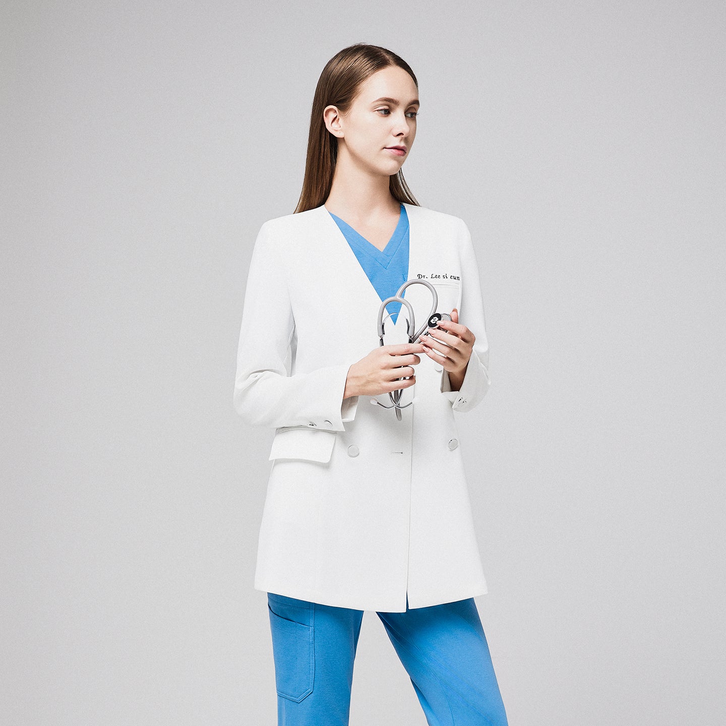 Female doctor in a white double-breasted lab coat, blue scrubs, holding a stethoscope, standing in a side pose,White