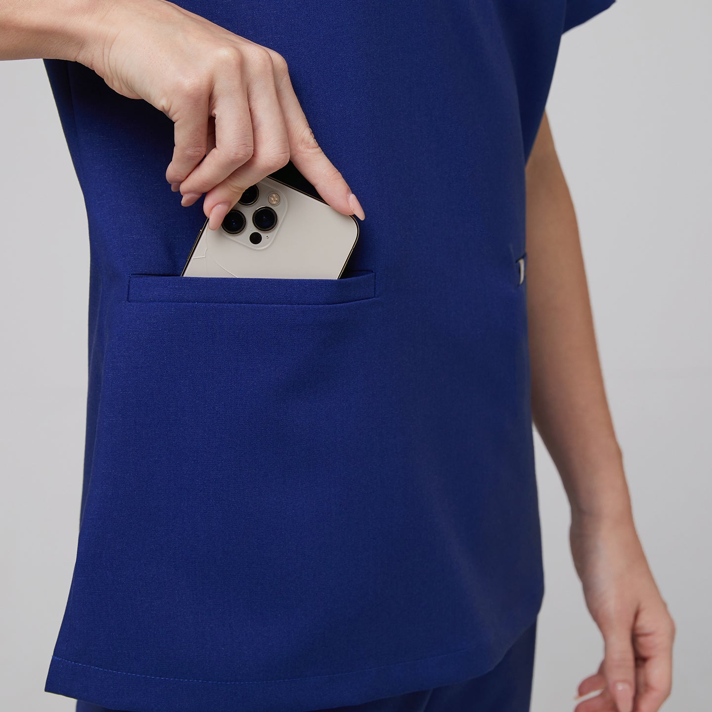 Close-up of a model placing a smartphone into the front pocket of a navy blue double pocket scrub top,Admiral Blue