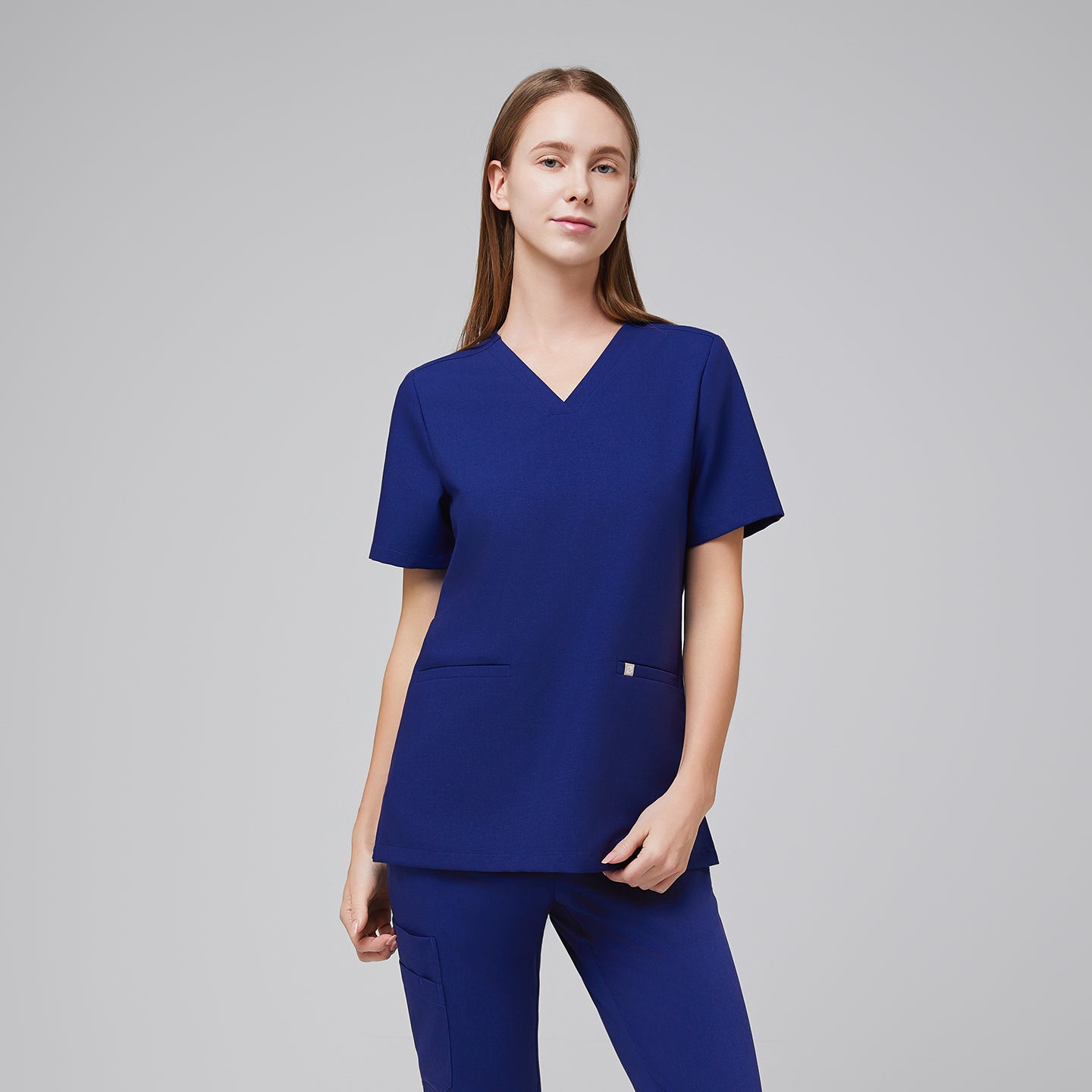 Woman wearing a navy blue V-neck scrub top with short sleeves, two front pockets, and matching pants,Admiral Blue