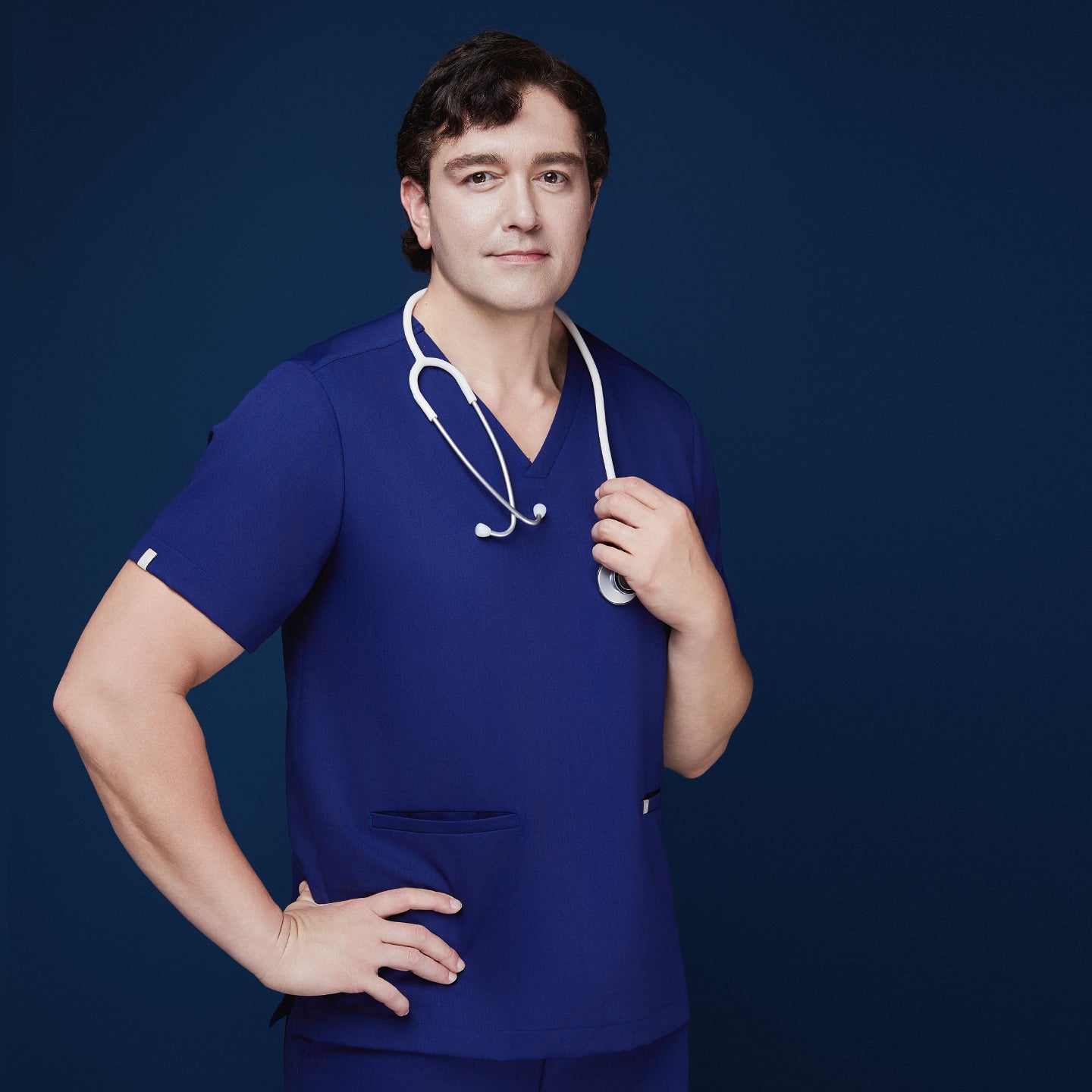 Man wearing admiral blue V-neck scrubs with double pockets, holding a white stethoscope over his shoulder, posing confidently,Admiral Blue