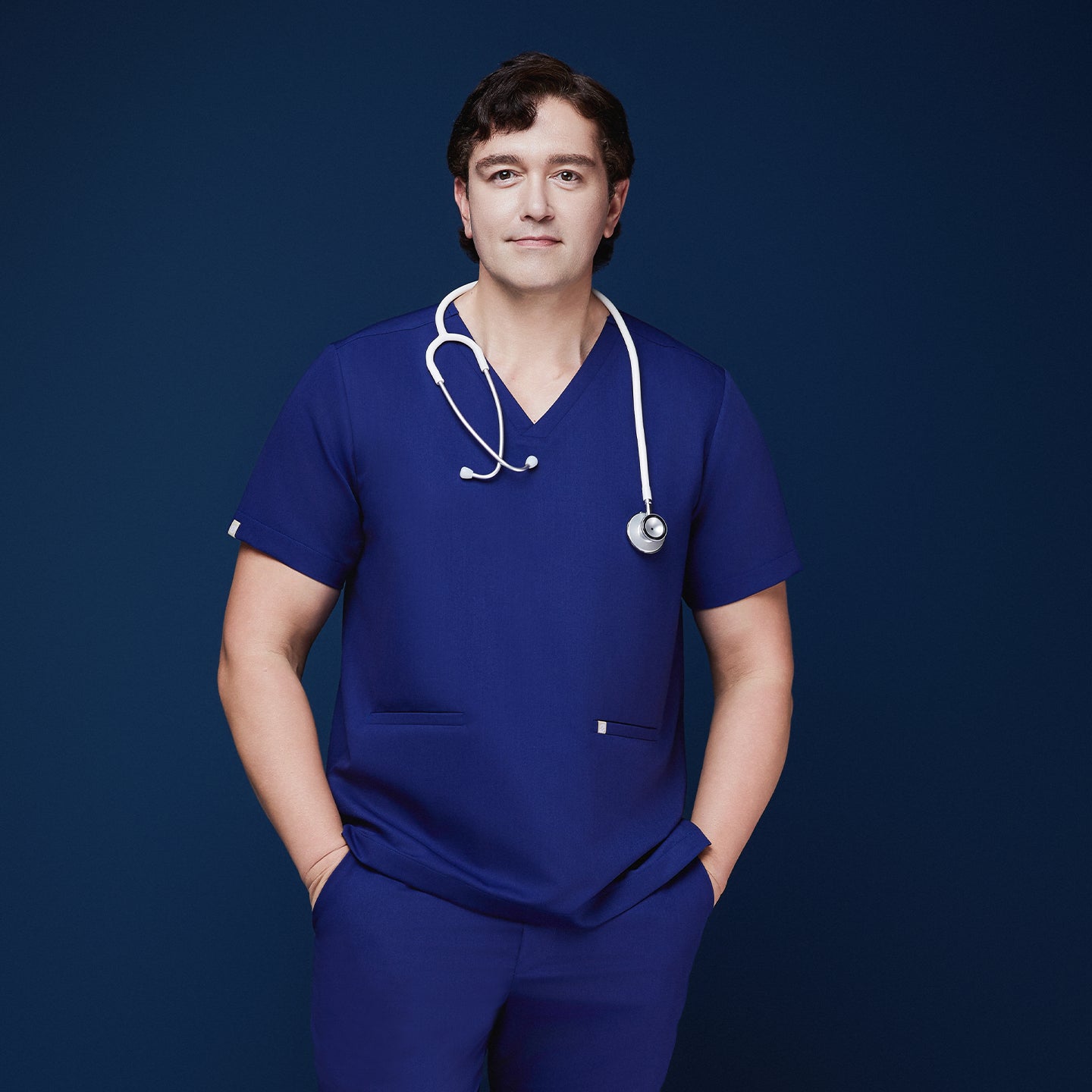 Male model in admiral blue scrub top with V-neck and double pockets, accessorized with a white stethoscope,Admiral Blue