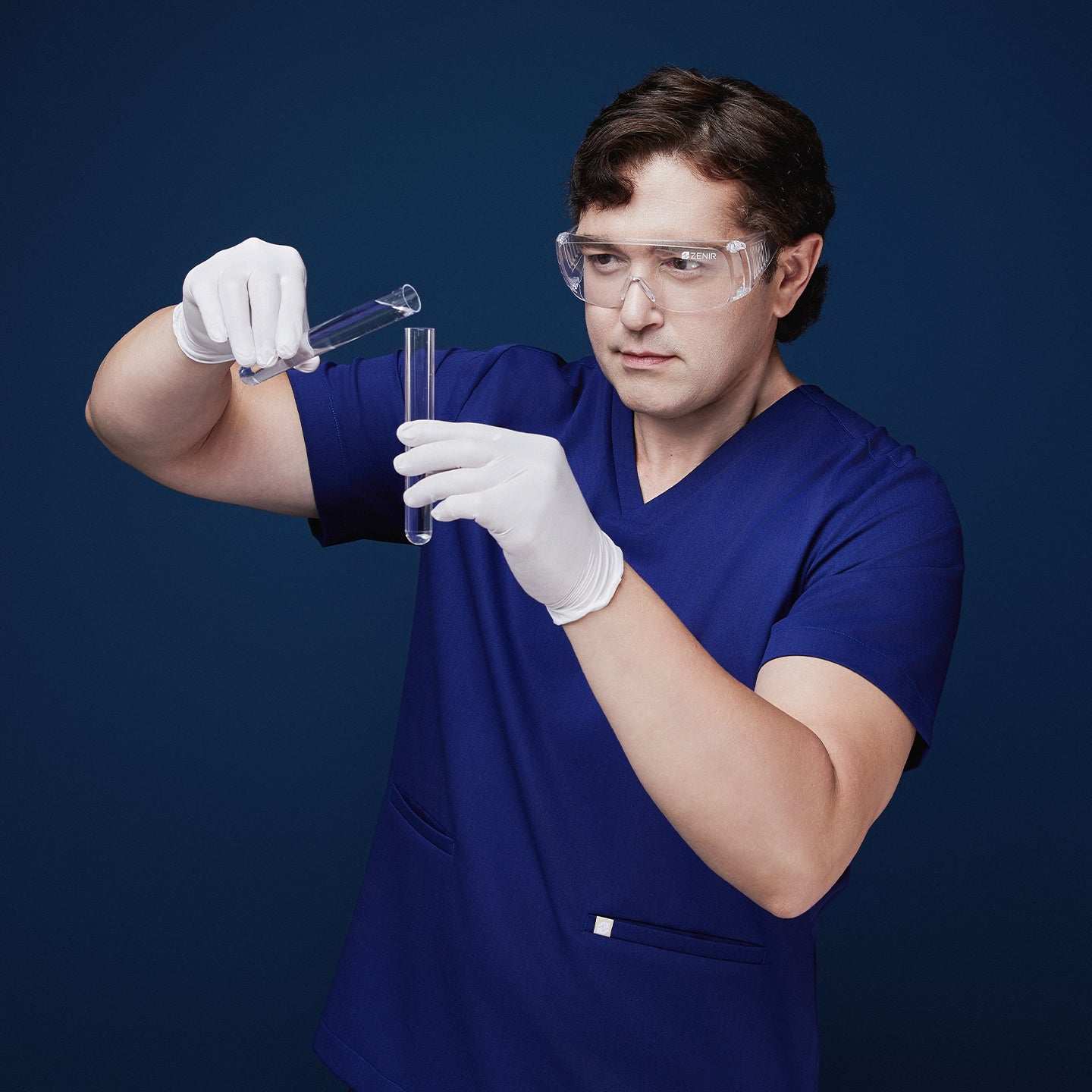 Man in admiral blue scrubs conducting a lab experiment, wearing safety goggles and gloves while handling test tubes,Admiral Blue