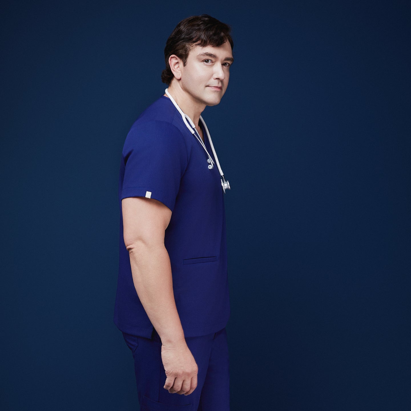 Man wearing admiral blue scrubs with V-neck and double pockets, holding a white stethoscope around his neck,Admiral Blue