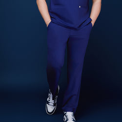 Image of Model showcasing admiral blue scrub pants with hands in pockets, paired with sneakers, standing against a navy backdrop,Admiral Blue