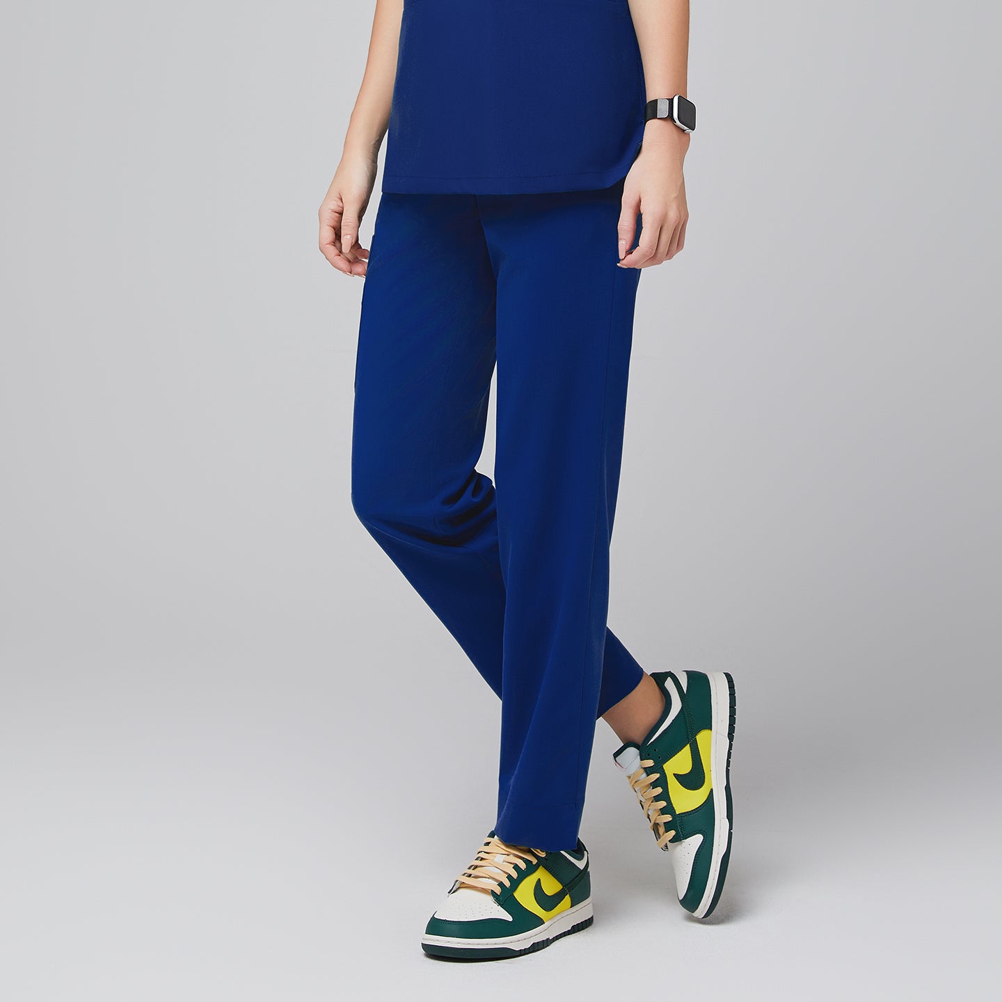 Female wearing blue scrub pants, shown from the side, paired with green, yellow, and white sneakers,Admiral Blue