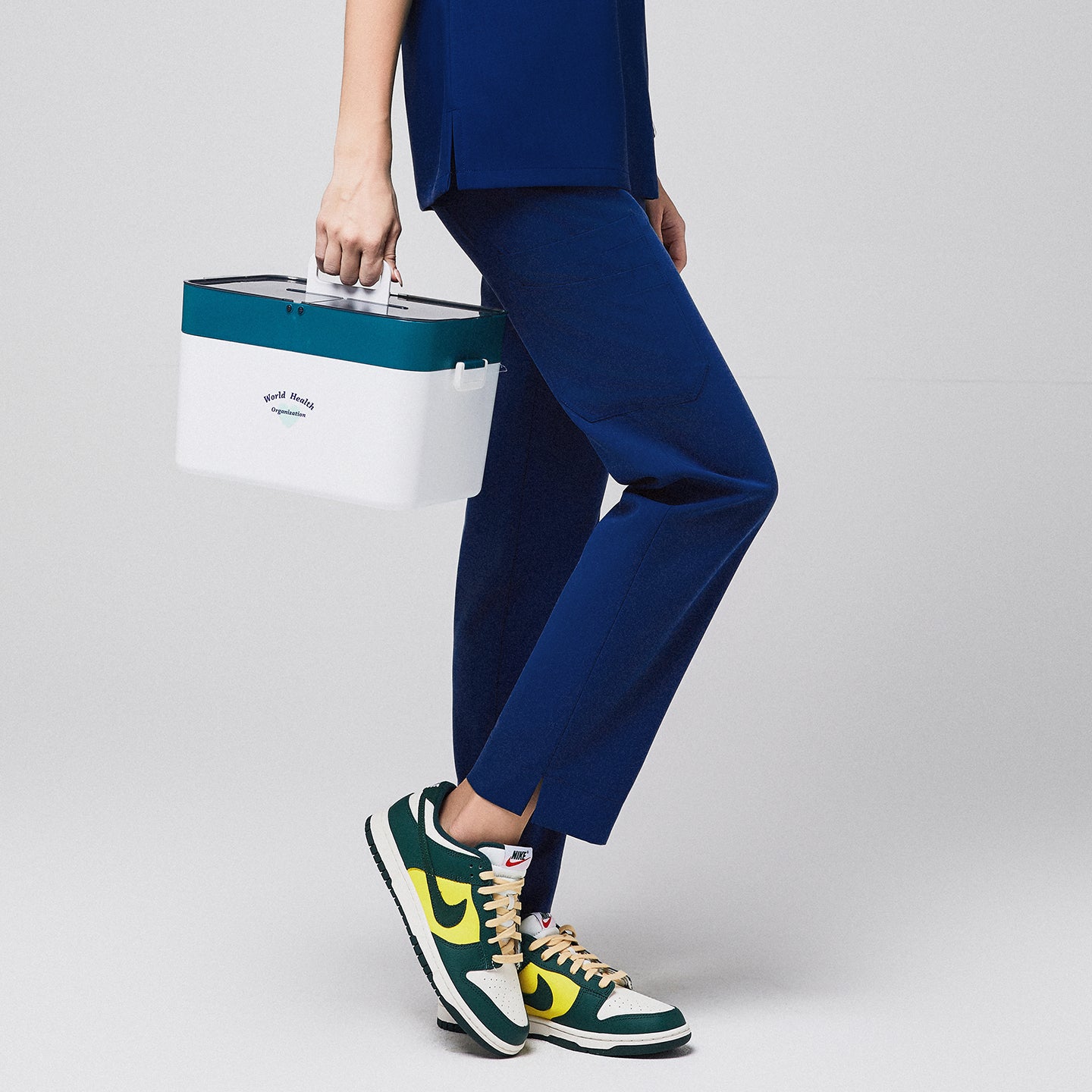 Admiral blue scrub pants with split hem and side pocket, carrying a white and teal World Health Organization container, paired with green and yellow sneakers,Admirial Blue