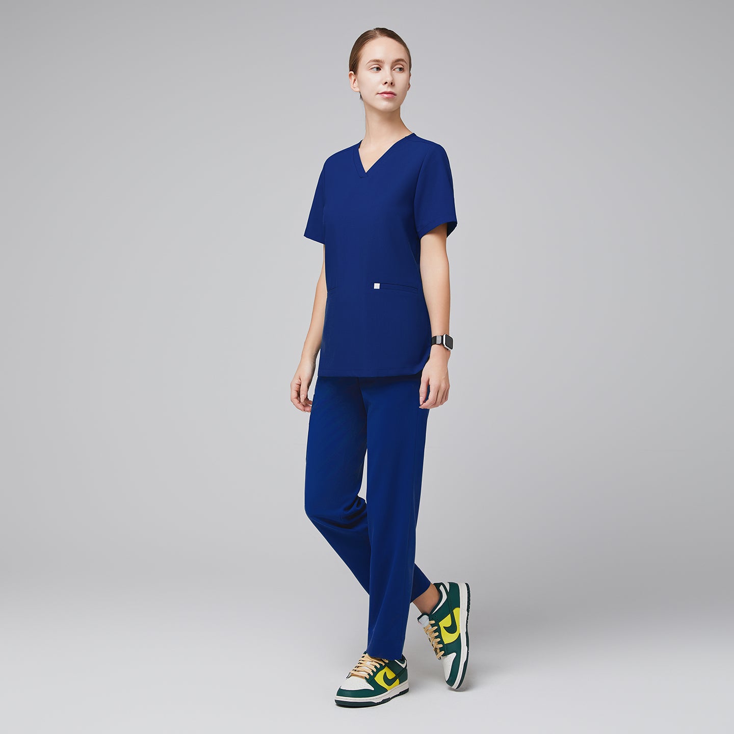 Female wearing blue scrub top and pants, standing in a side pose, paired with green, yellow, and white sneakers,Admiral Blue