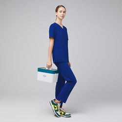 Image of Female model in blue scrub top and pants, holding a white and teal medical box, paired with green, yellow, and white sneakers,Admiral Blue