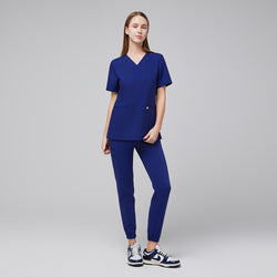 Image of Model wearing admiral blue jogger scrub pants with elastic cuffs and a matching V-neck scrub top, paired with white and blue Nike sneakers,Admiral Blue