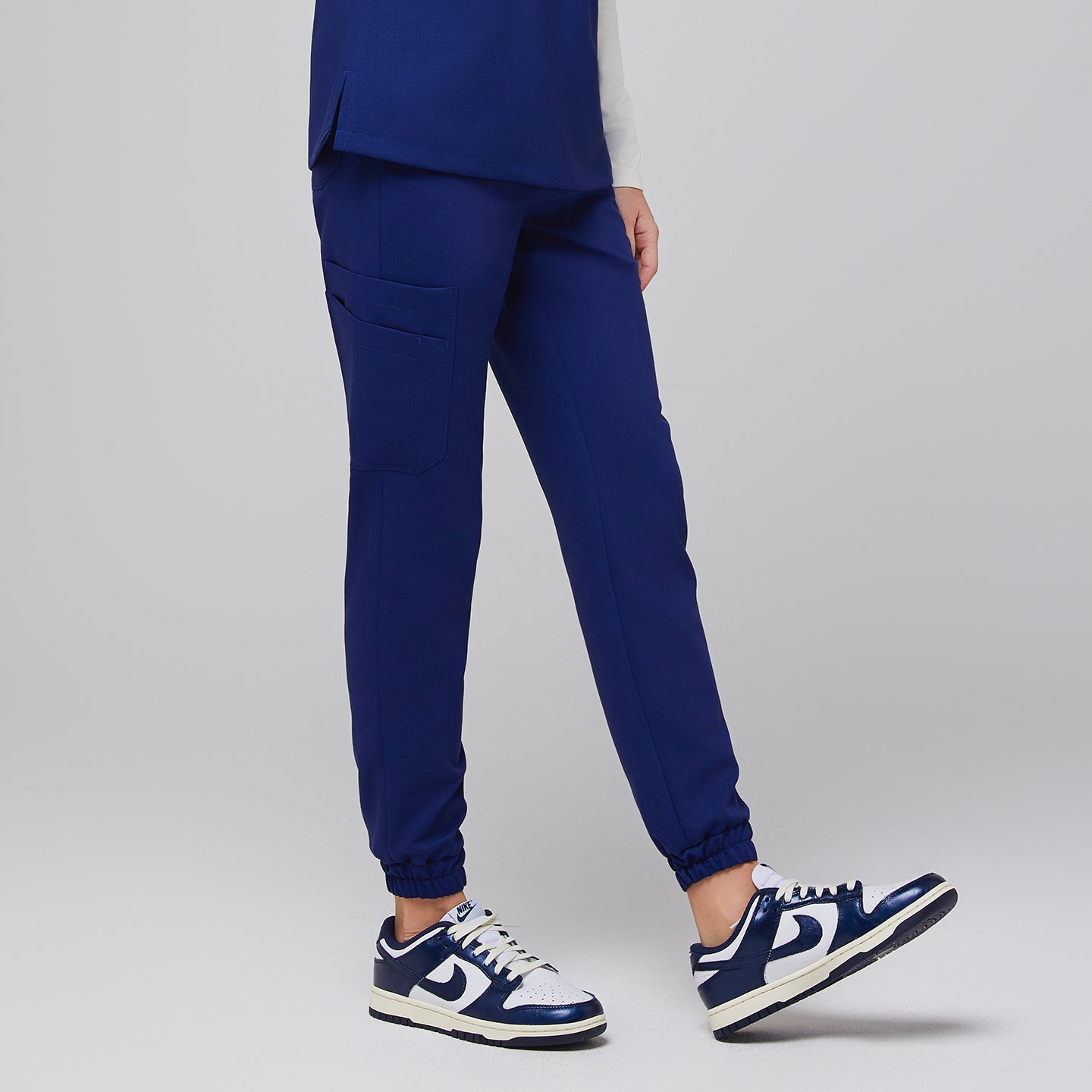 Admiral blue jogger scrub pants with cargo pocket and elastic cuffs, shown in a dynamic side pose with white and blue Nike sneakers,Admiral Blue