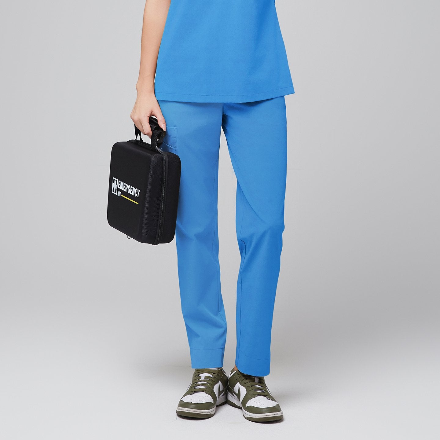 Close-up of a model wearing aqua blue scrub pants ft, holding a black emergency kit against a grey background,Aqua Blue