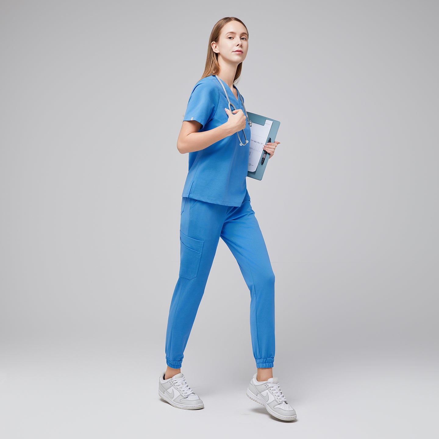 Side view of a woman in aqua blue jogger scrubs holding a clipboard and stethoscope, wearing white sneakers,Aqua Blue