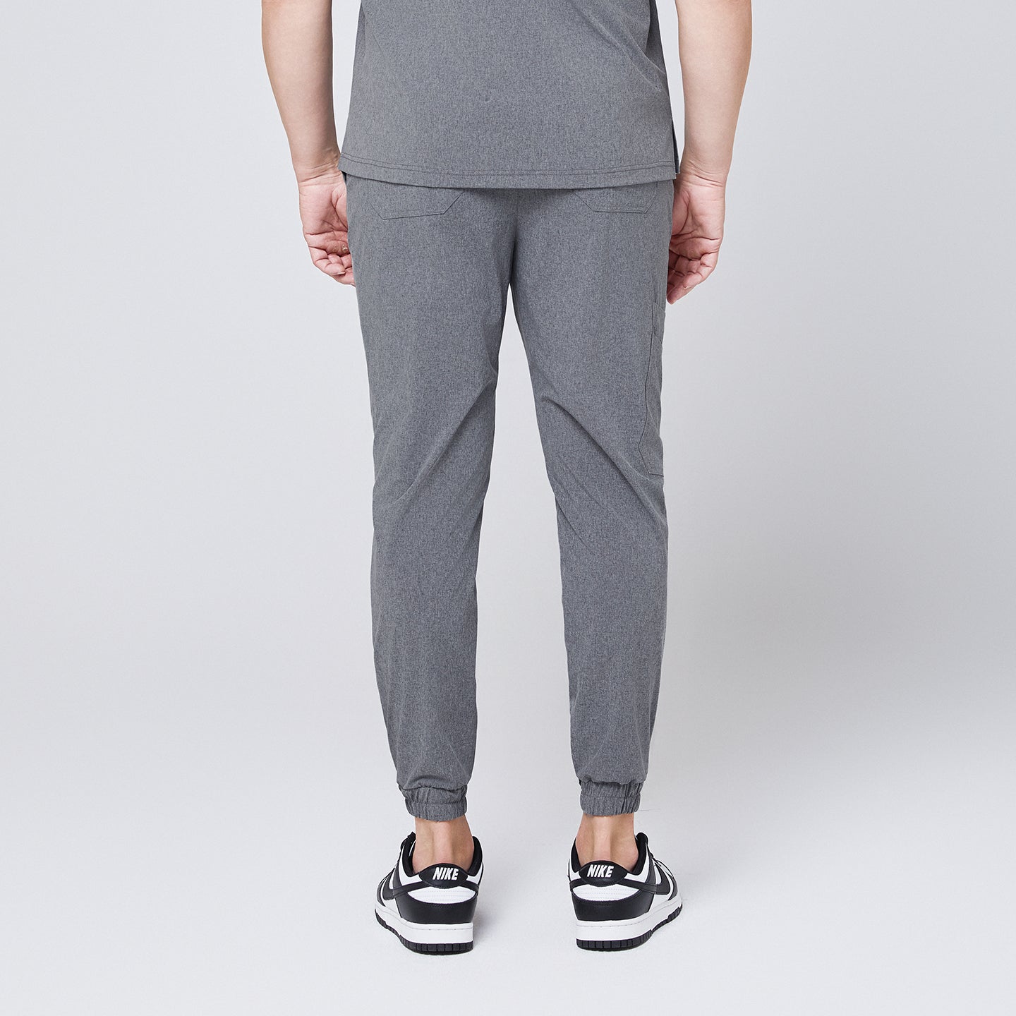 Back view of ash gray jogger scrub pants with elastic cuffs and back pockets, styled with black and white sneakers,Ash Gray