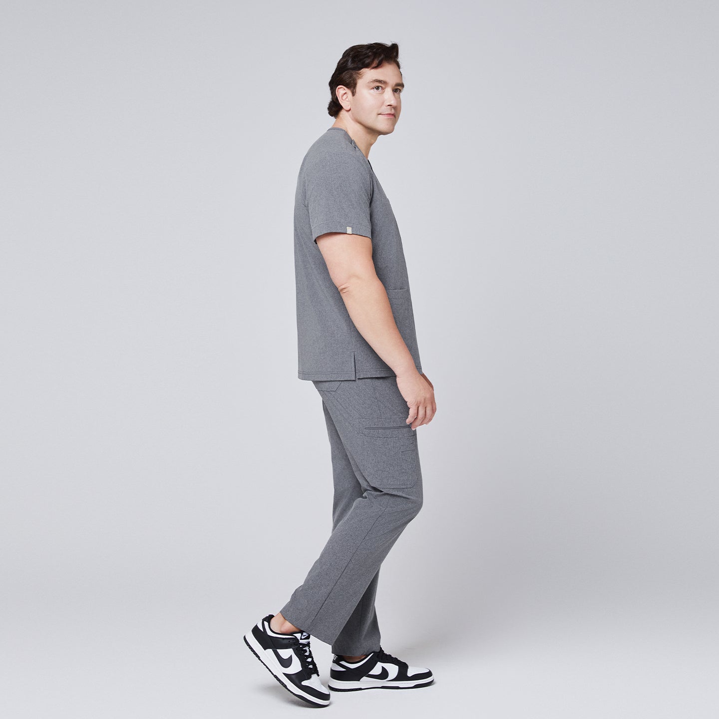 Male model in side profile wearing an ash gray scrub set with black and white sneakers, showcasing clean lines and functional design,Ash Gray