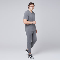 Image of Male model in ash gray scrub top with shoulder buttons and jogger-style pants, posing in black and white sneakers,Ash Gray