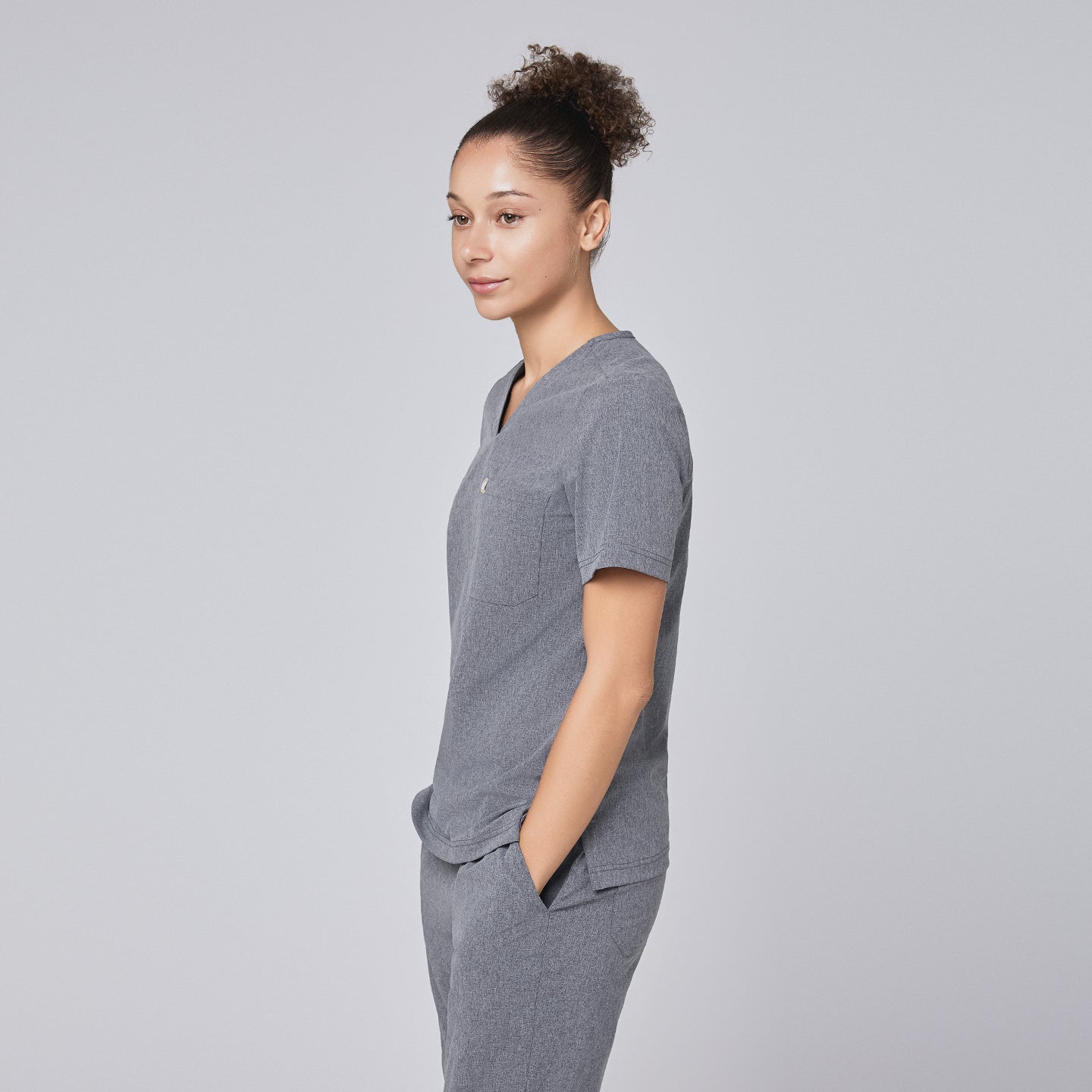 Side profile of a healthcare professional wearing an ash gray scrub set with hands in pockets, standing confidently against a light gray background,Ash Gray