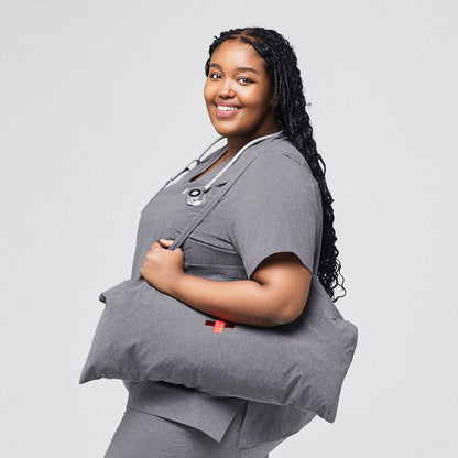 Healthcare worker in ash gray scrub top carrying a bag and wearing a stethoscope, side view, smiling,Ash Gray