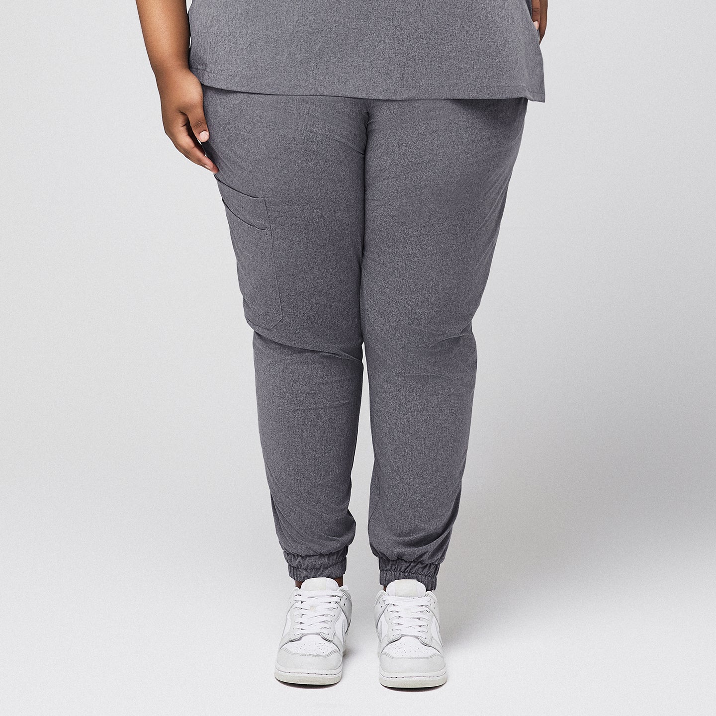 Plus-size ash gray jogger scrub pants with elastic cuffs, cargo pocket, and stretch fit, paired with white sneakers on neutral background,Ash Gray