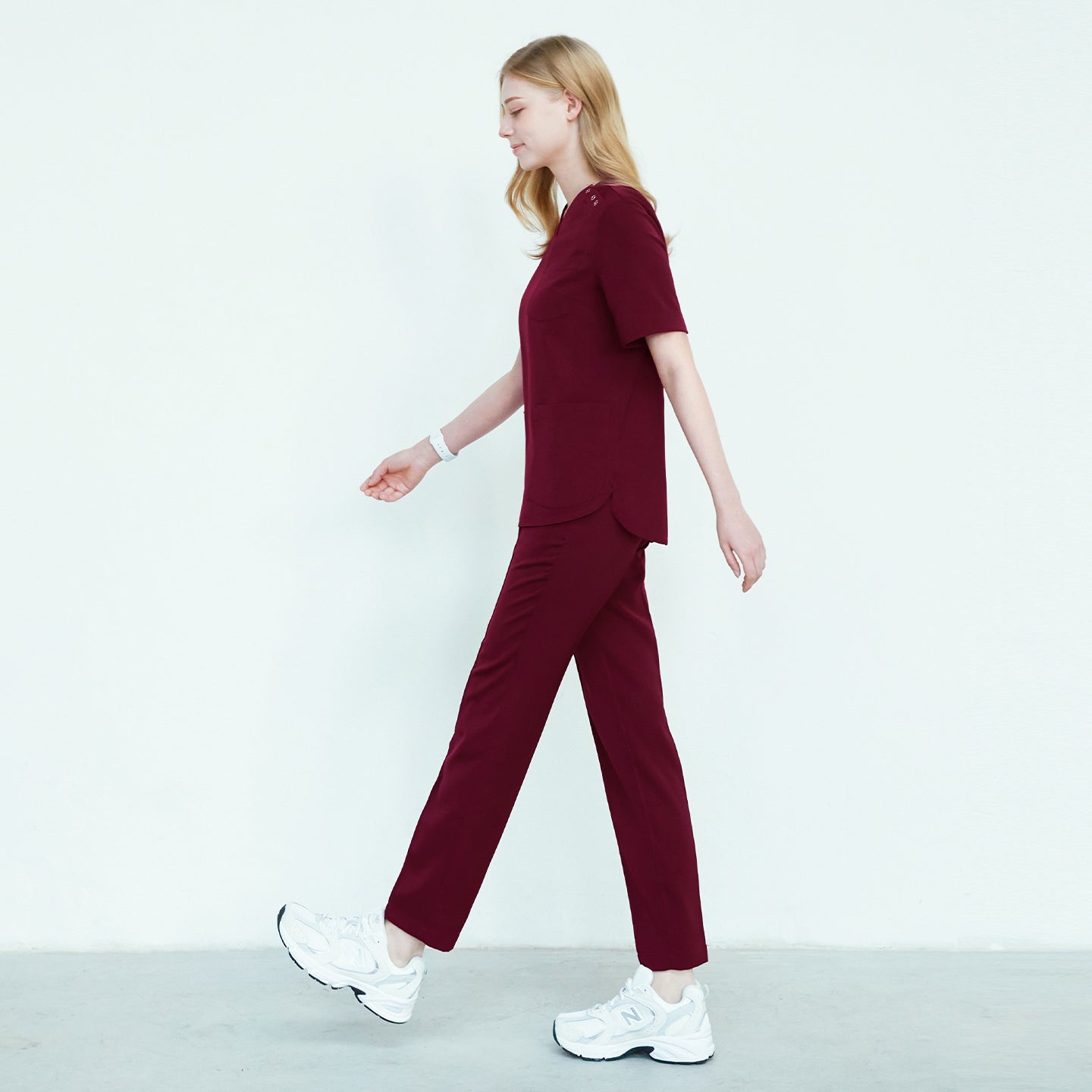 Female model in burgundy scrub top and pants, walking in a side view, wearing white sneakers,Burgundy