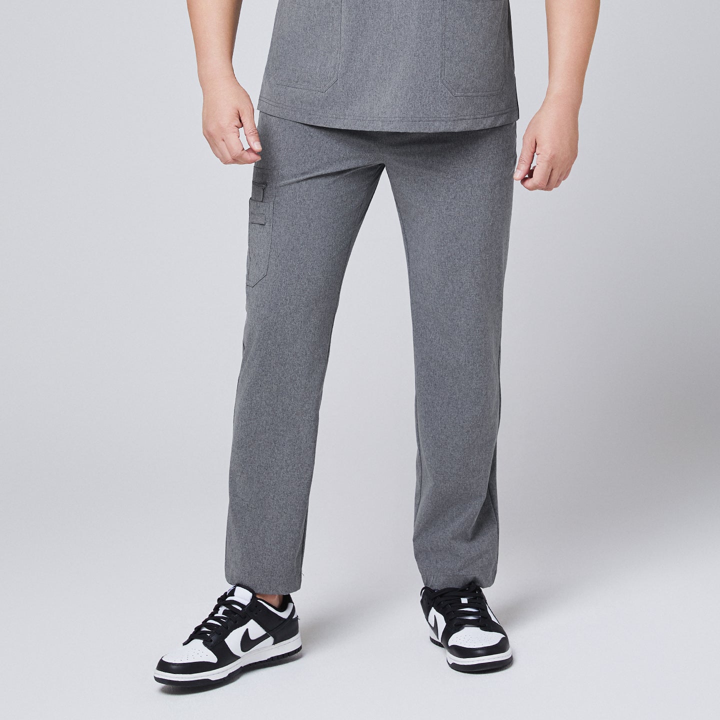 Male model wearing ash gray relaxed-fit scrub pants with side pockets, paired with black and white sneakers, presenting a comfortable and professional medical look,Ash Gray