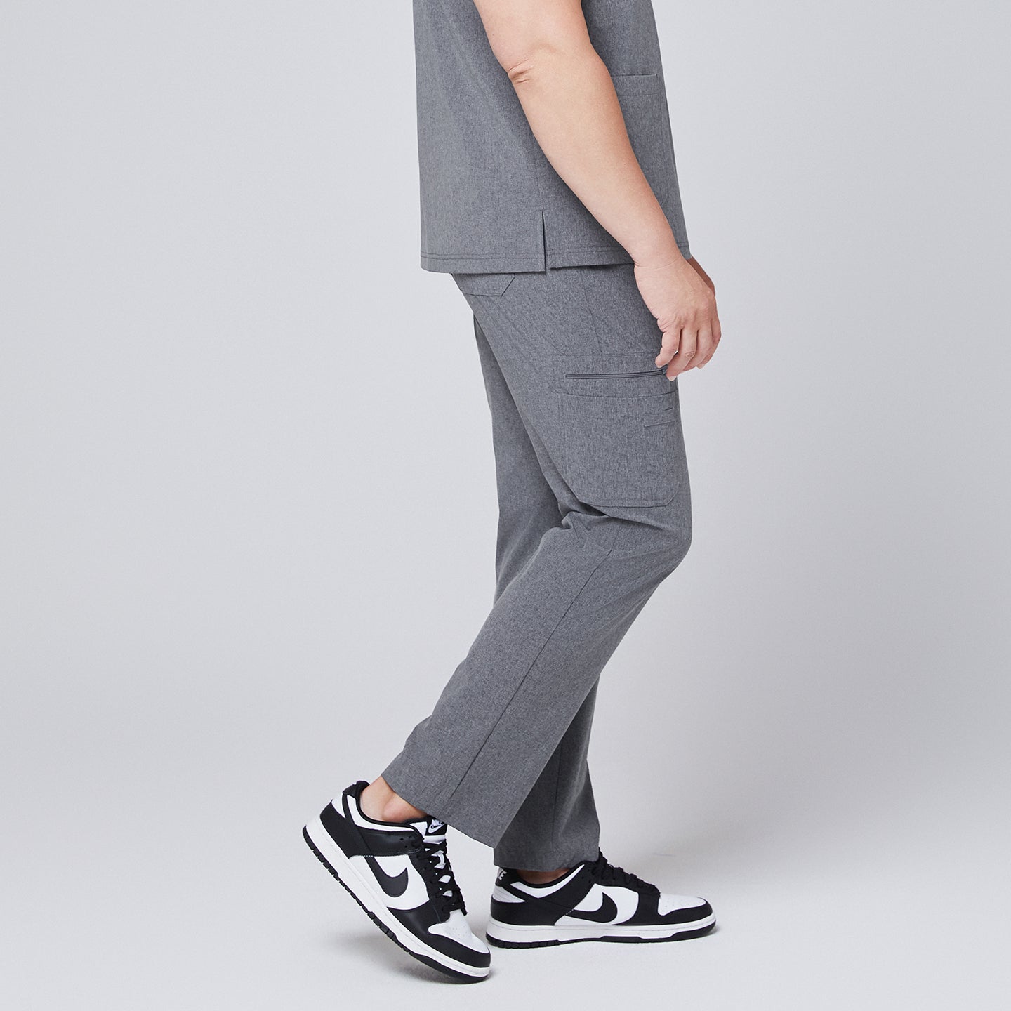 Male model showcasing ash gray relaxed-fit scrub pants with functional side pockets, styled with black and white sneakers, highlighting a side profile for a sleek and professional look,Ash Gray