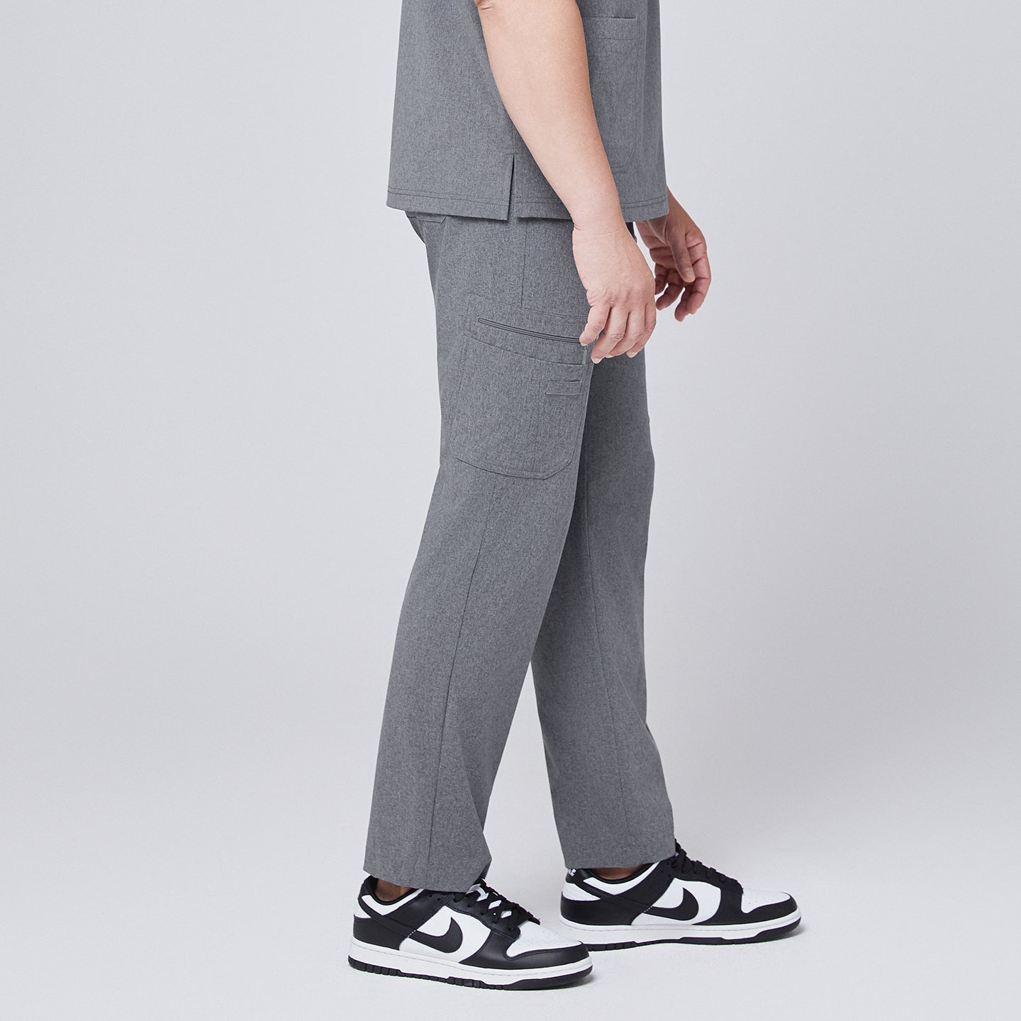 Male model wearing ash gray relaxed-fit scrub pants with side pockets, styled with black and white sneakers, showcasing a side angle for a modern and functional look,Ash Gray