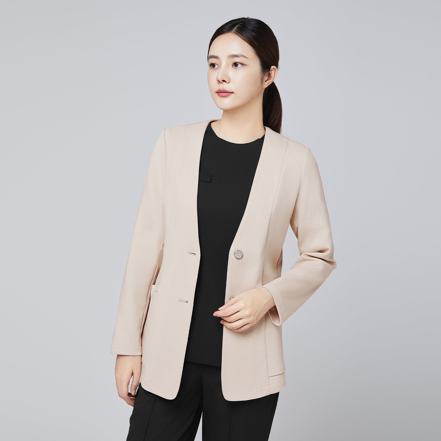 A professional woman wearing a beige comfort cardigan over a sleek black top and trousers, styled with her hair tied back, looking poised against a neutral background,Beige