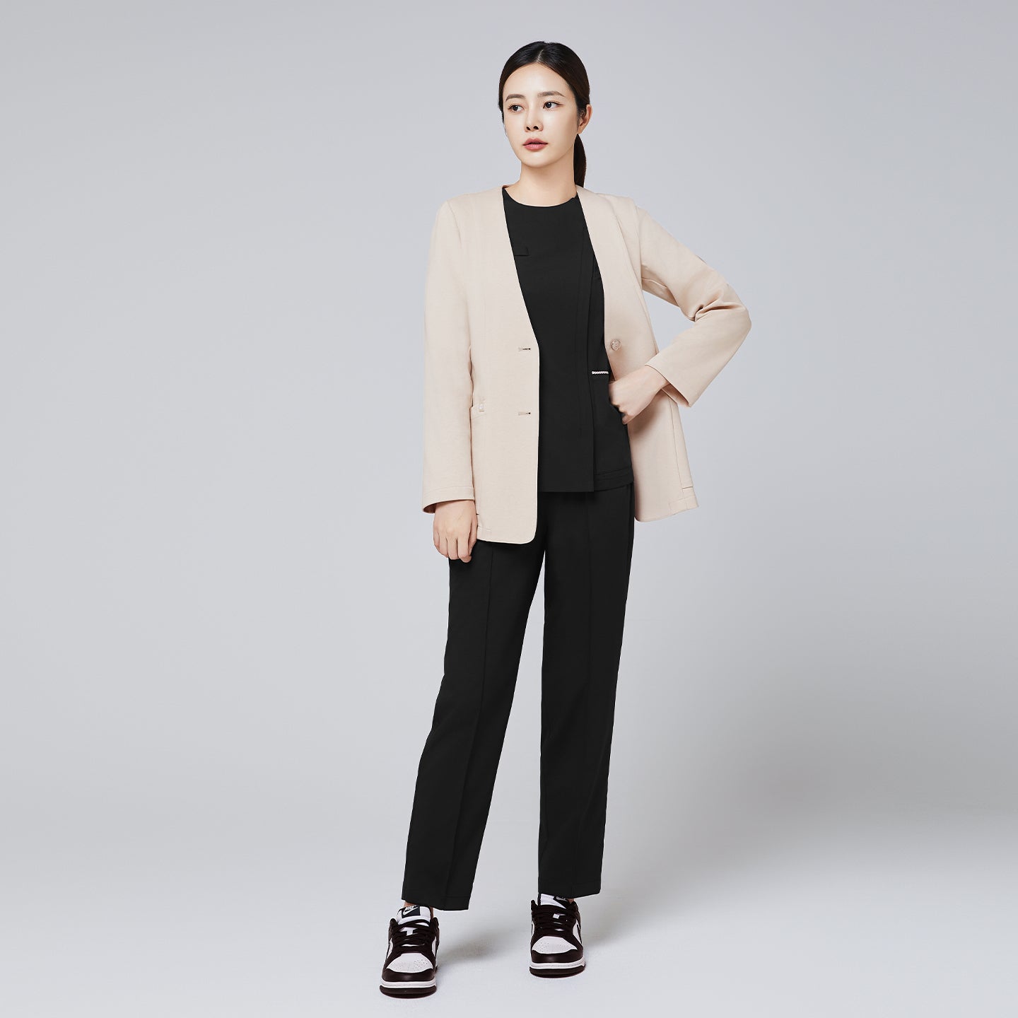 A professional woman dressed in a beige comfort cardigan over a black top and trousers, paired with stylish black-and-white sneakers, standing confidently against a neutral background,Beige