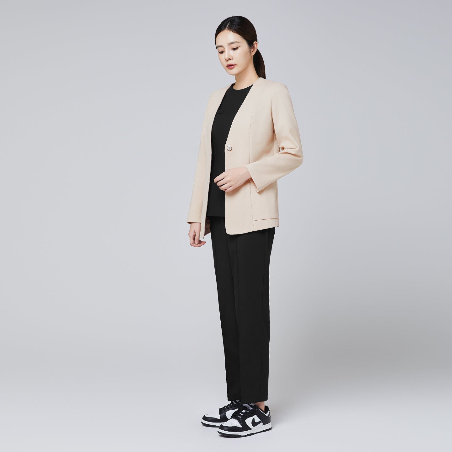 A woman dressed in a beige comfort cardigan paired with black trousers and stylish sneakers, posing elegantly in a full-body side profile against a plain background,Beige