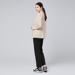 Image of A woman wearing a beige comfort cardigan and black trousers, posing in a rear three-quarter view with her head turned toward the camera, styled with sleek sneakers and a ponytail against a plain background,Beige