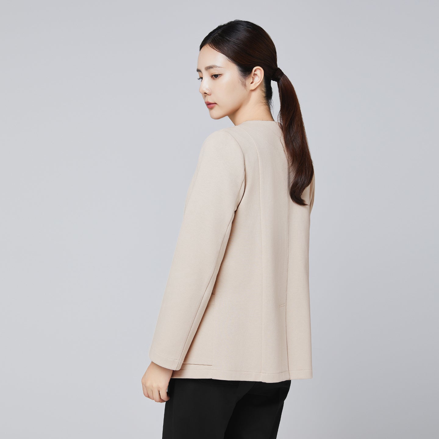 A professional woman wearing a beige comfort cardigan over a sleek black top and trousers, styled with her hair tied back, looking poised against a neutral background,Beige