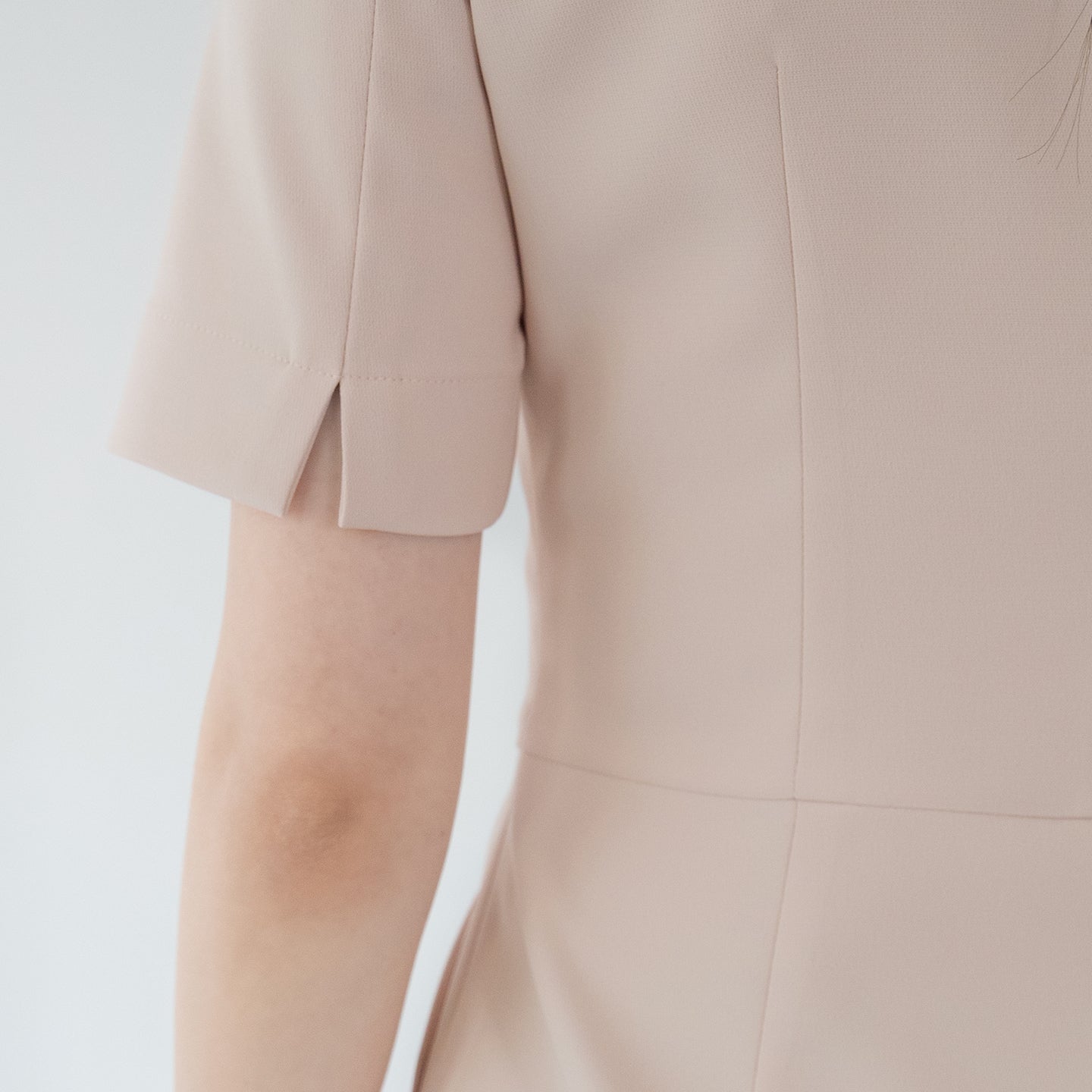 A close-up of a beige round-neck top's sleeve, highlighting the back slit detail on the short sleeve,Beige