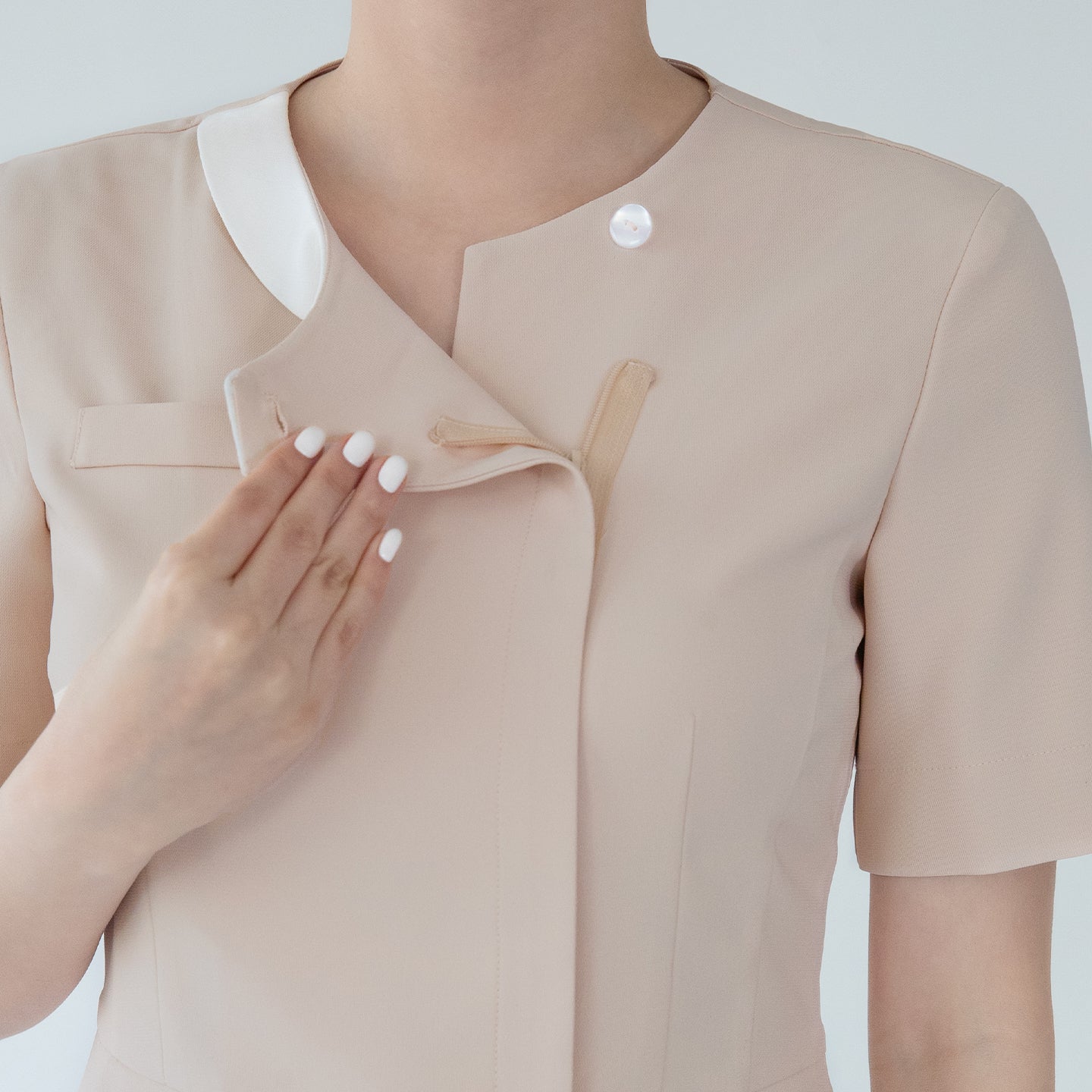 A close-up of a beige round-neck top with a front zipper and button detail, showing a hand opening the zipper to reveal the inner layer,Beige