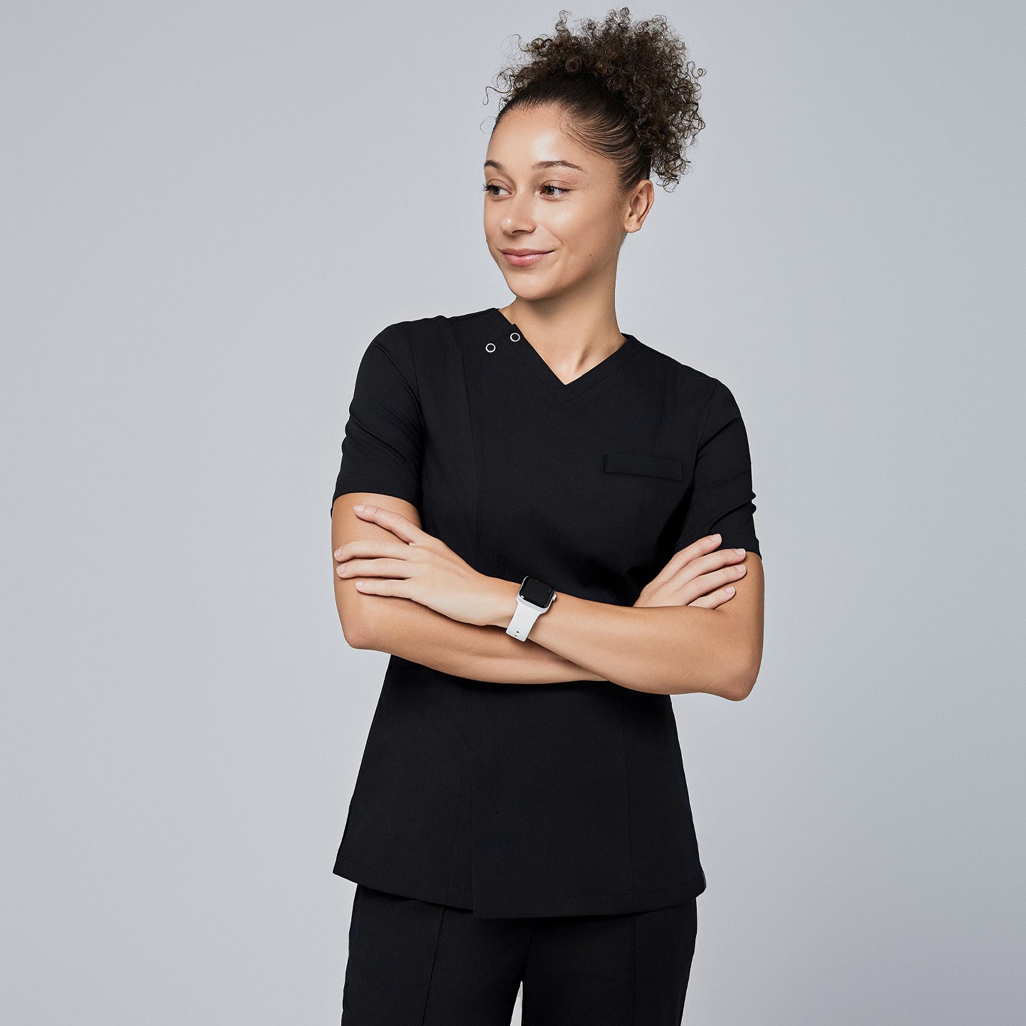 Female model wearing a black V-neck scrub top with a front zipper and short sleeves, standing with arms crossed and smiling,Eco Black