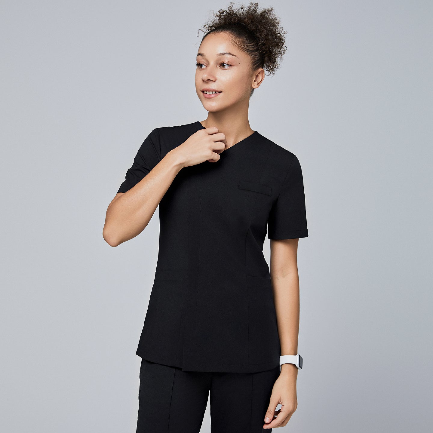 Female model wearing a black V-neck scrub top with a front zipper and short sleeves, smiling and holding the collar with one hand,Eco Black