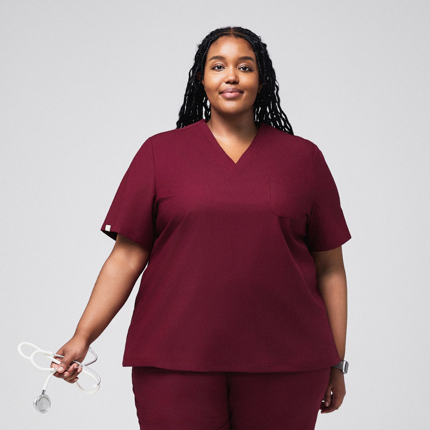 Woman wearing a burgundy scrub top and matching pants, holding a stethoscope,Burgundy