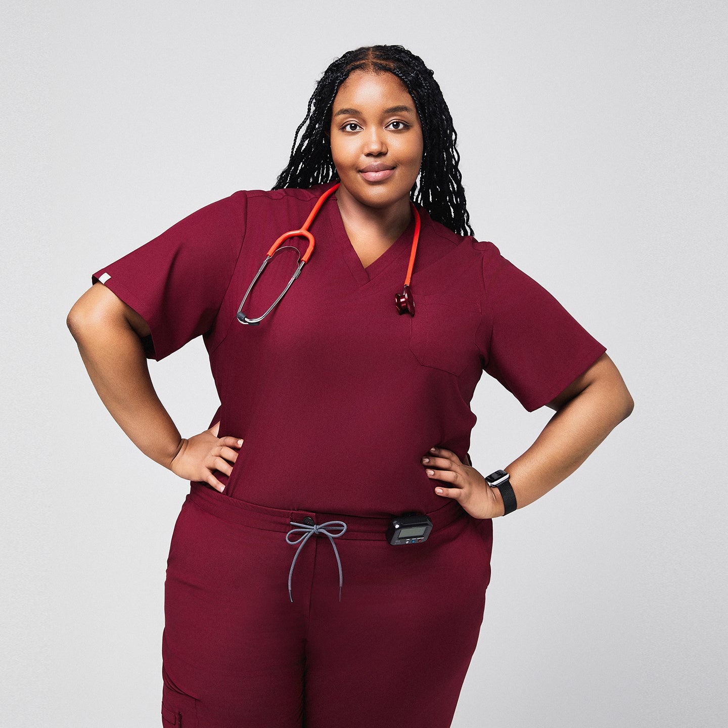 Confident plus-size model wearing a burgundy 3-pocket scrub top and drawstring pants, accessorized with a red stethoscope and smartwatch, perfect for healthcare professionals,Burgundy