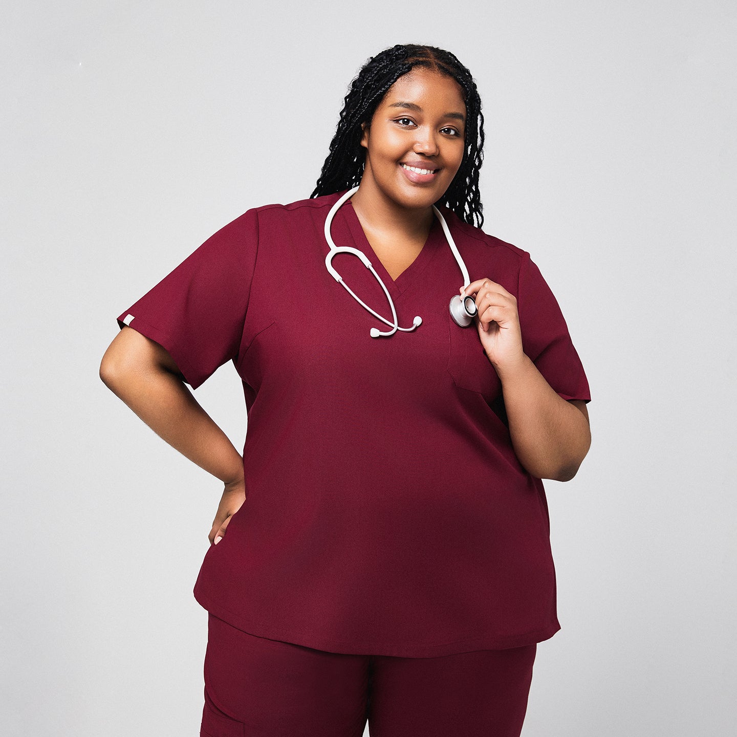 Plus-size model wearing a burgundy 3-pocket scrub top, holding a gray stethoscope, showcasing a professional and comfortable look for medical environments,Burgundy