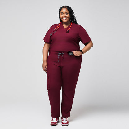 Plus-size model wearing a burgundy 3-pocket scrub top and matching pants, paired with red sneakers, featuring a comfortable and functional design ideal for medical professionals,Burgundy