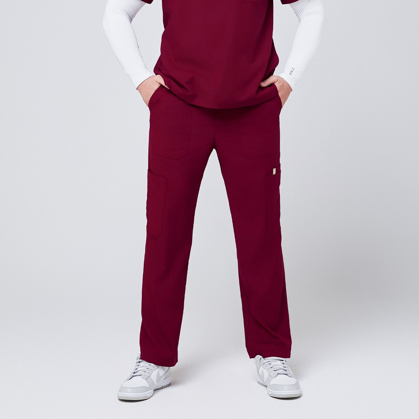 Close-up of burgundy 8-pocket straight scrub pants paired with a matching scrub top and white sneakers,Burgundy