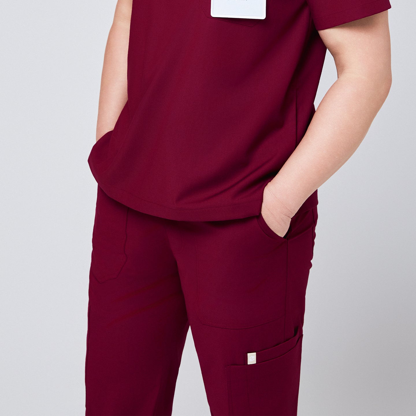 Close-up of burgundy scrub pants with multiple pockets and matching scrub top, featuring hands in pockets for functionality,Burgundy