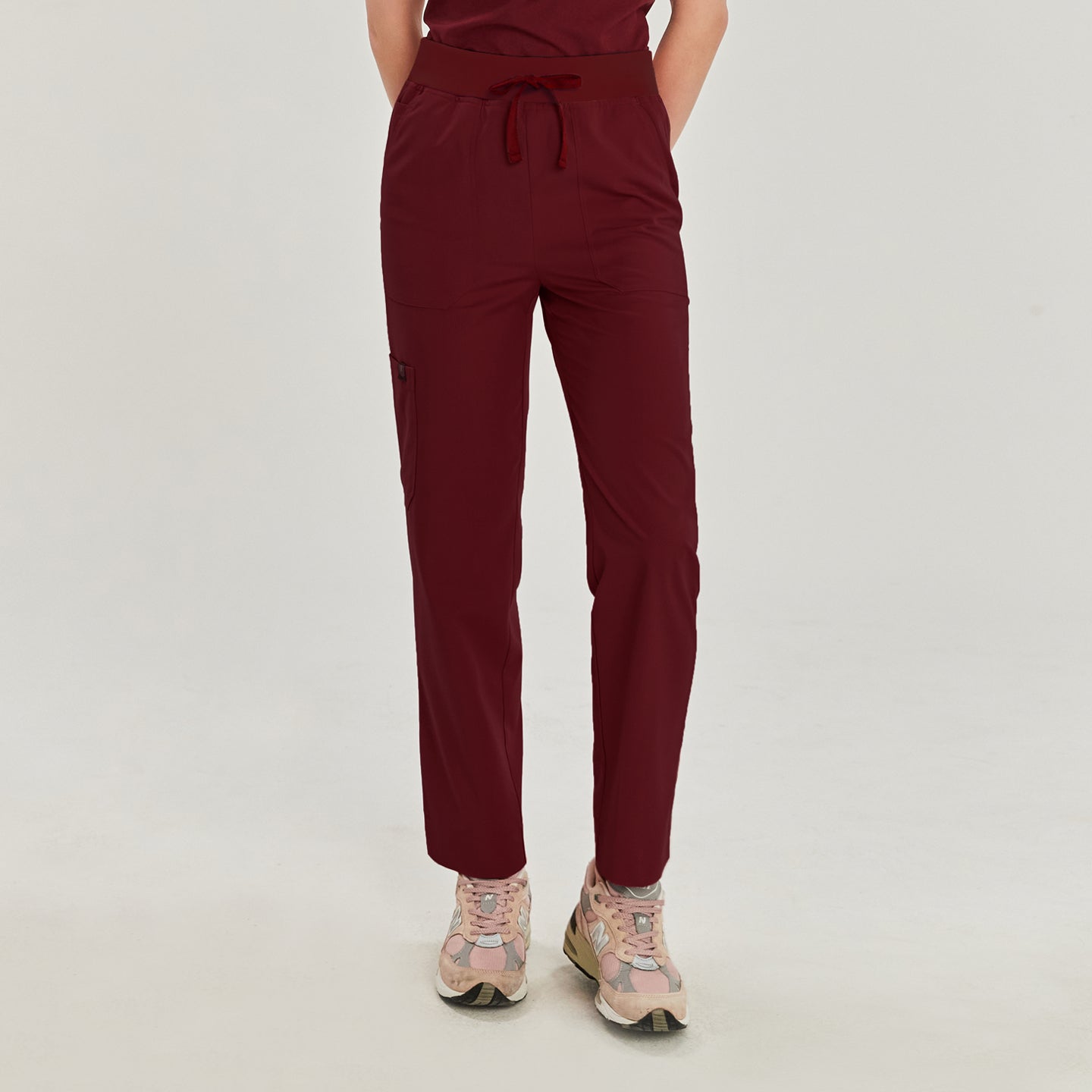 Front view of a woman wearing burgundy zipper slit scrub pants with a drawstring waist and side pocket, paired with pink sneakers,Burgundy