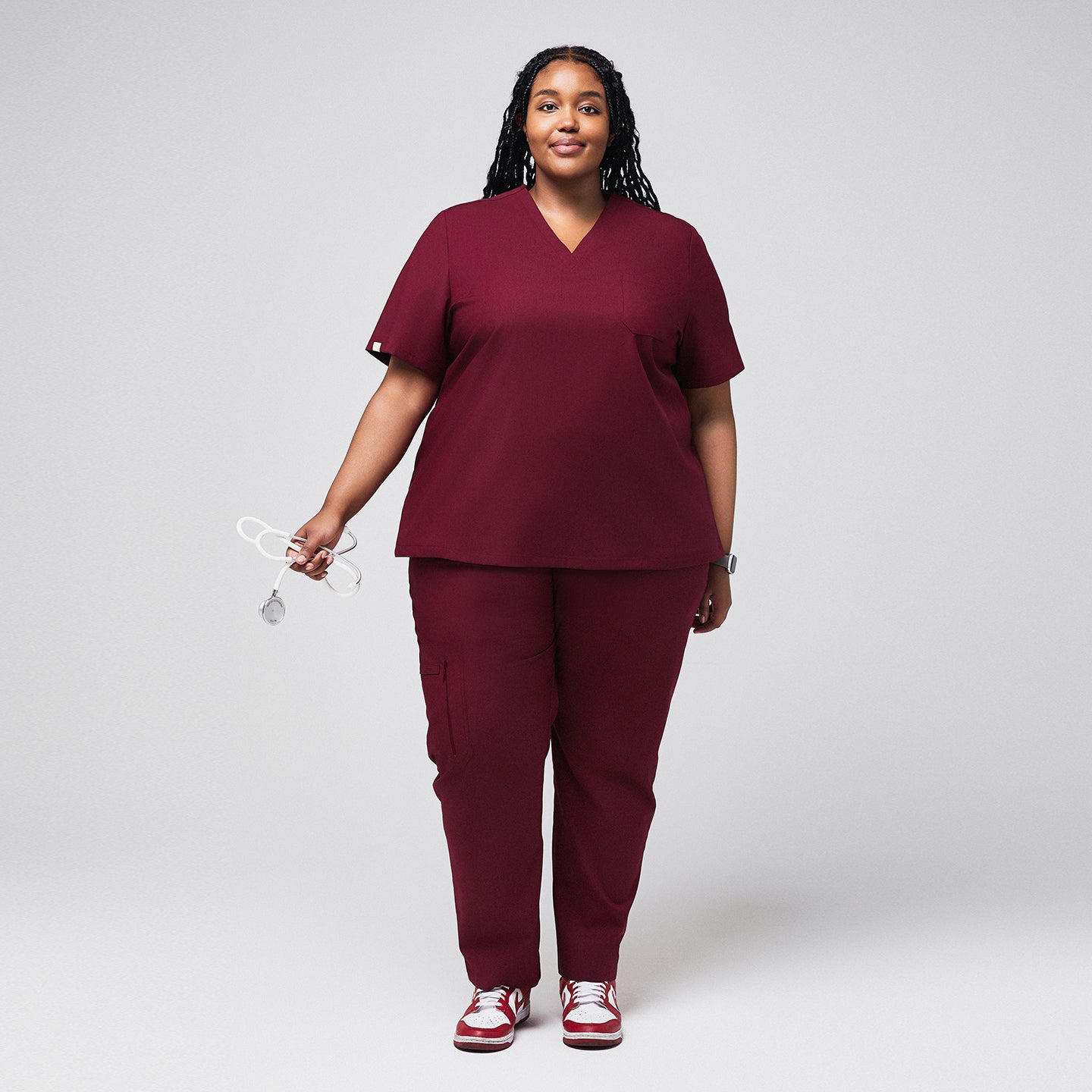 Plus-size healthcare professional in burgundy scrubs with zipper pocket pants, holding a stethoscope and smiling,Burgundy