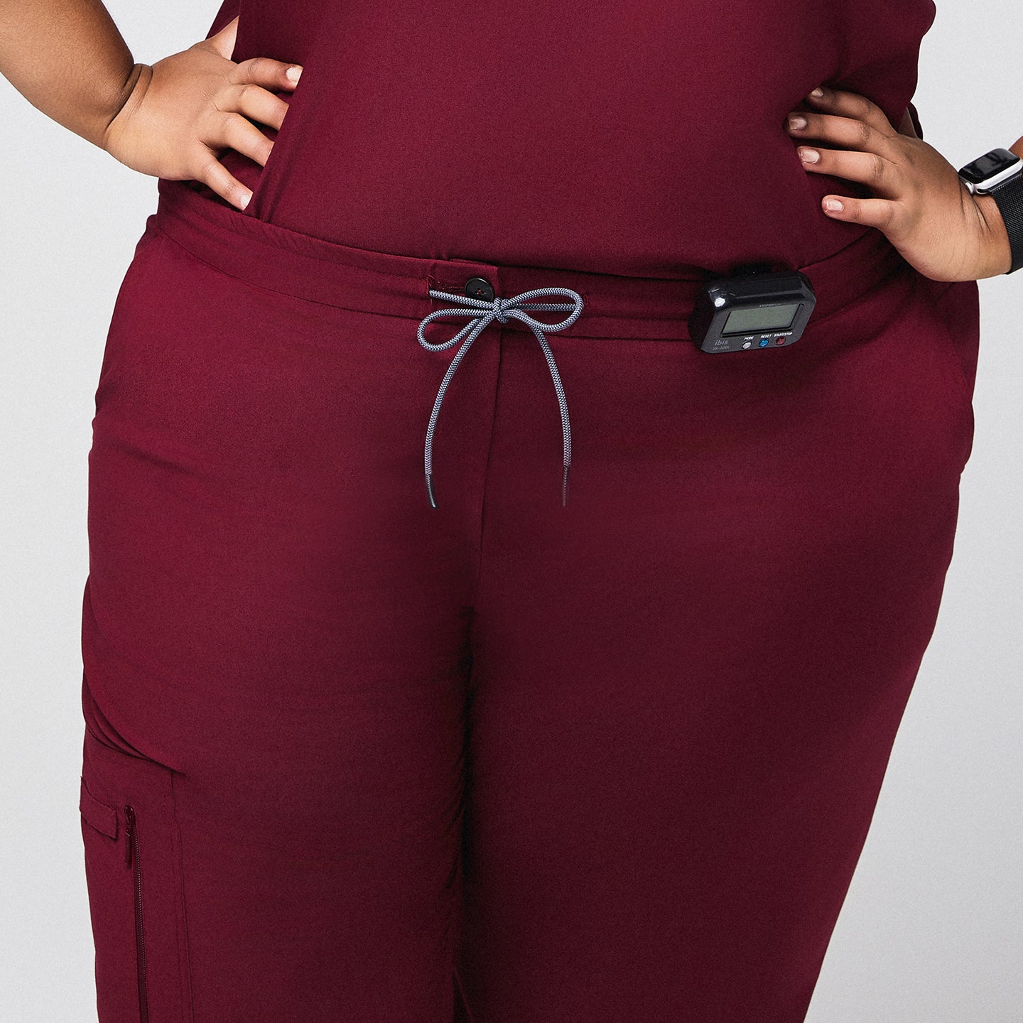 Burgundy scrub pants with drawstring waist and zipper pocket, featuring a medical device clipped at the waist,Burgundy