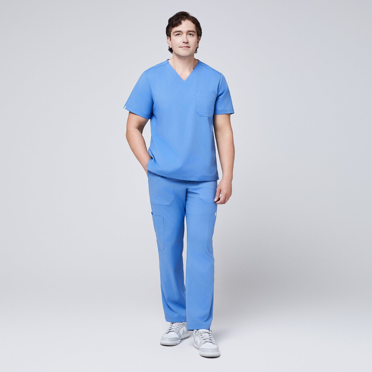 Male model wearing a ceil blue V-neck scrub set with a three-pocket top and straight-leg pants, paired with white sneakers for a clean, professional look,Ceil Blue