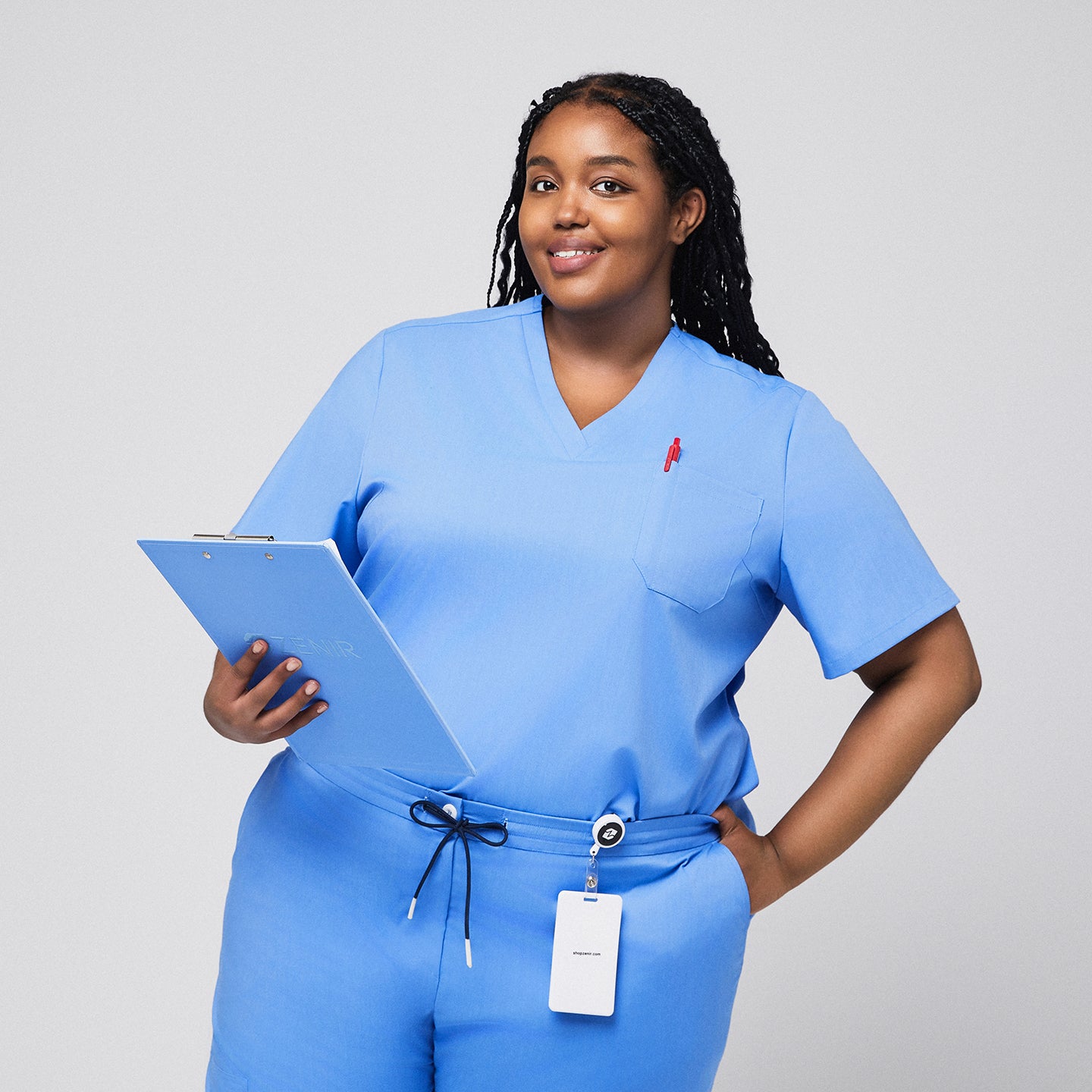 Plus-size model wearing a light blue 3-pocket scrub top, holding a clipboard with badge holder attached, ideal for medical professionals,Ceil Blue